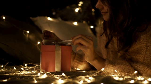 年轻快乐的女人在圣诞装饰房间里拿她的圣诞礼物的特写。圣诞彩灯环绕着她。锅了视频下载