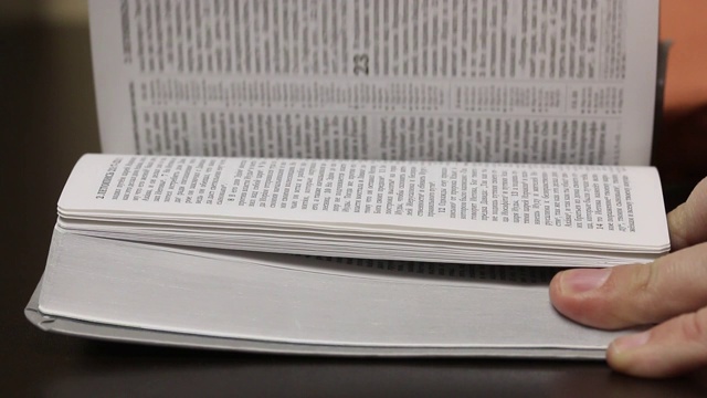 桌上放着一本打开的《圣经》。一个男人慢慢地翻着书页，寻找所需要的章节。特写镜头。视频素材