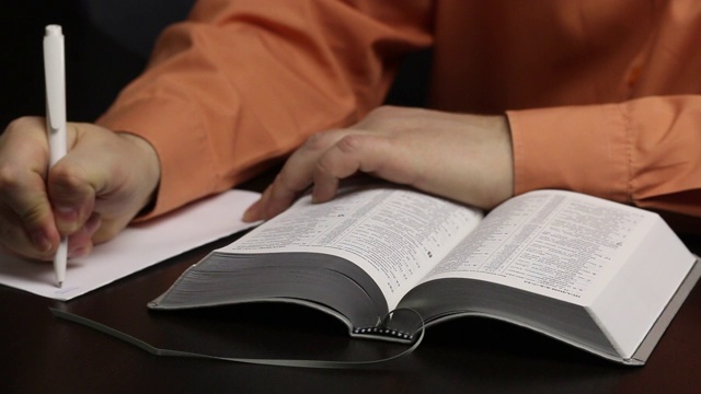 一个人坐在桌子旁读圣经。引导手指沿着线。把重要的想法写在一张纸上。特写镜头视频素材
