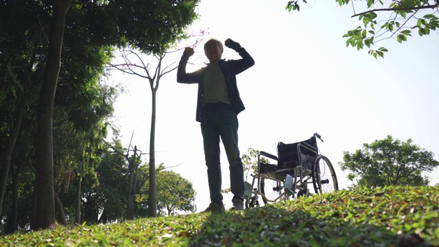 亚洲老人从户外公园的轮椅上站起来视频素材