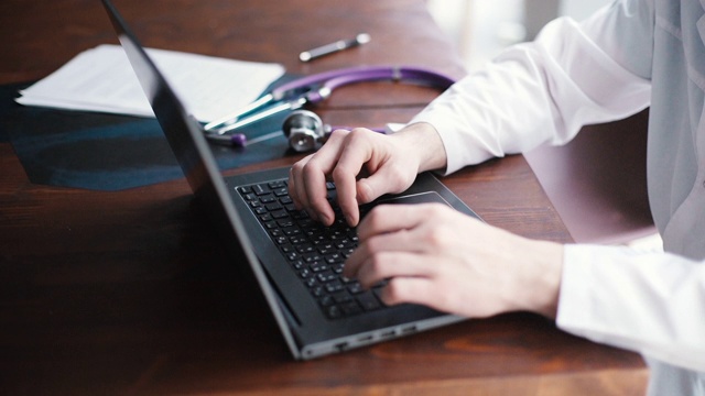 一名身穿白大褂的医生正在笔记本电脑上打字，特写。视频素材