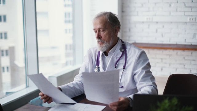 经验丰富的高加索成年医生坐在桌子前研究病人报告视频素材