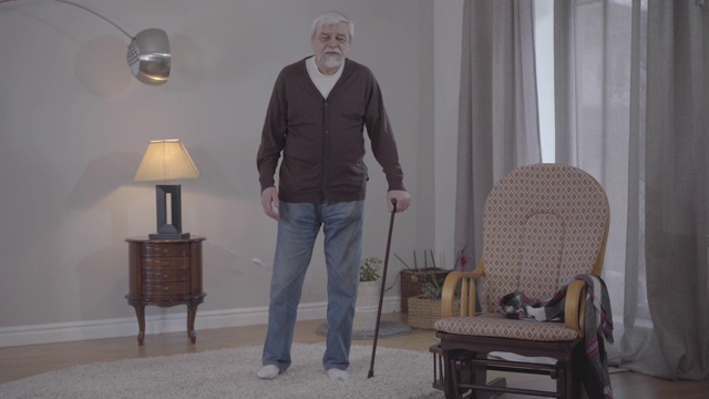 这是一幅白人老人拿着手杖在家听音乐的画像。广泛的镜头积极的退休享受晚上室内。生活方式，快乐，爱好，幸福。视频素材