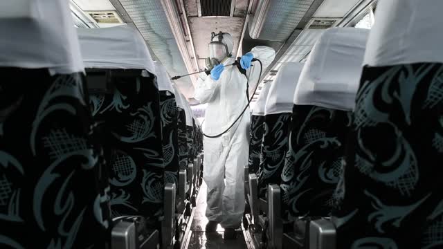 工作人员戴着防护口罩，穿着防护服，正在用冠状病毒喷雾器对巴士内部进行消毒视频下载