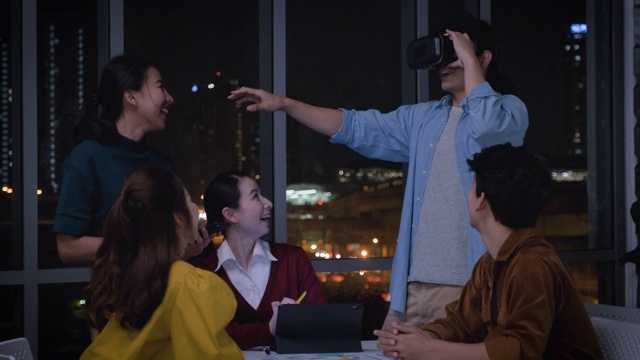 亚洲用户体验开发人员和ui设计师在夜晚的城市灯光下，在现代办公室中使用手机应用原型设计虚拟现实眼镜。创意数字发展机构视频素材