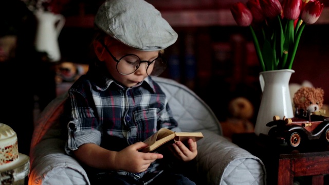 可爱的蹒跚学步的小男孩，戴着眼镜，看书，喝茶吃饼干视频素材