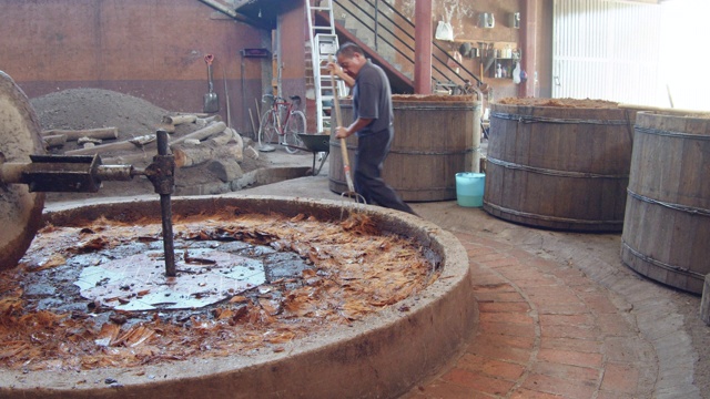 传统马磨石磨龙舌兰芯。自制mezcal生产。用干草叉的男人。前台放着发酵龙舌兰的木桶视频下载