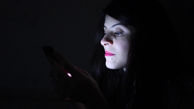 一个女人在黑暗中独自使用智能手机视频下载