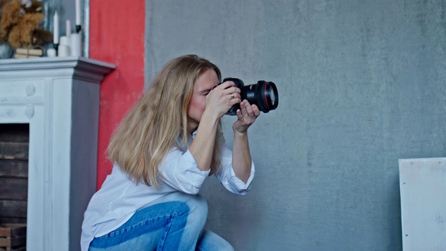 美丽的女孩摄影师对准画框，手里拿着相机。女孩在摄影棚里拍照，她很开心。视频下载