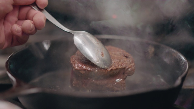 SLO MO:专业厨师用勺子在铸铁平底锅里翻动牛排视频素材