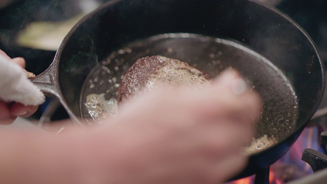 SLO MO:专业厨师用勺子将黄油融化在铸铁平底锅里的牛排上视频下载