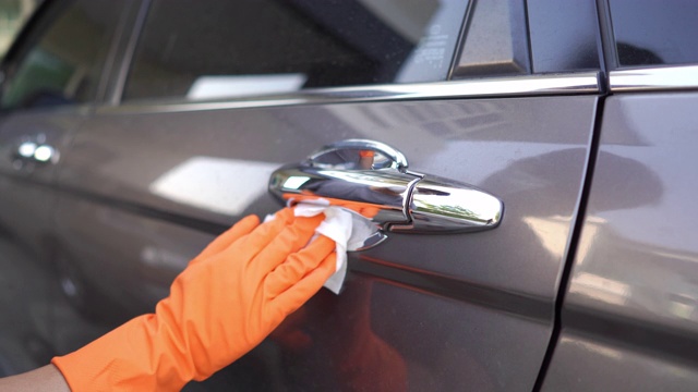 手戴手套在家中车库擦拭清洁covid-19病毒的灰色汽车门把手表面。视频素材