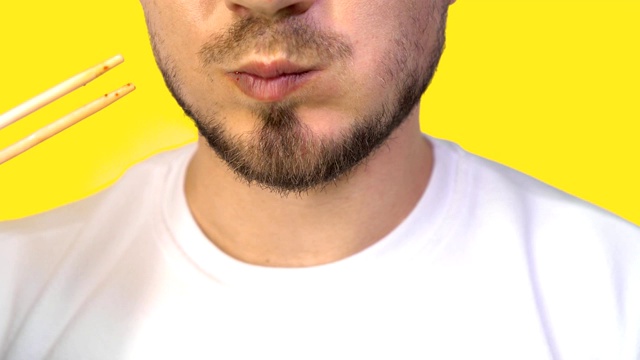 特写的男性嘴与刚毛在黄色固体背景。一个男人吃日本寿司，用筷子卷视频素材