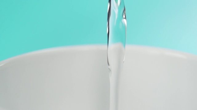 纯净的饮用水正从绿松石背景的绿色塑料瓶中倒入一个白色的杯子视频素材