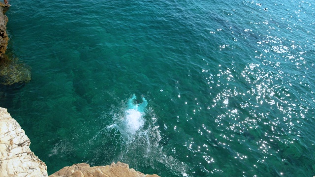 COPY SPACE:一个年轻人在暑假里在一个阳光明媚的日子里进行悬崖跳水。视频素材