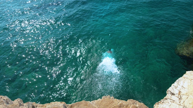 拷贝空间:一个人从岩石上跳下来，跳进闪闪发光的蓝色海洋。视频素材