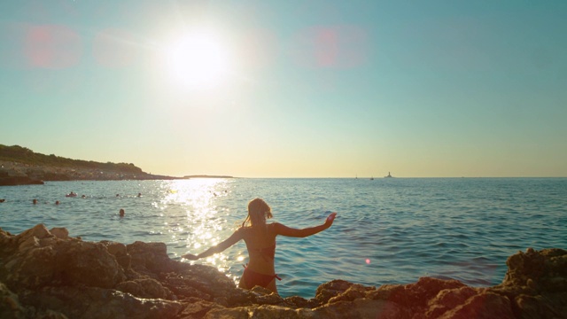 太阳耀斑:女孩从悬崖上跳下来，在跳进海里的时候踢回了腿。视频素材