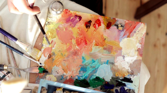 女画家在调色板上使用画笔，手的特写，俯视图混合油画颜料视频下载
