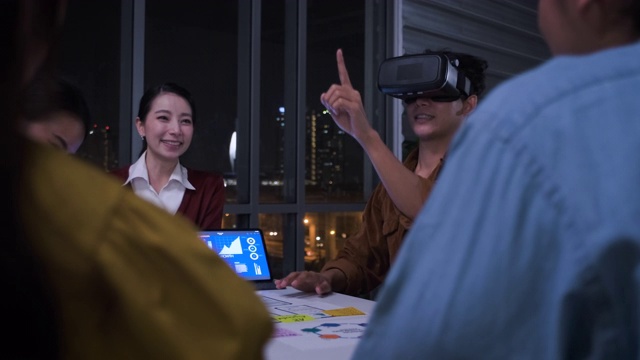 亚洲用户体验开发人员和ui设计师在夜晚的城市灯光下，在现代办公室中使用手机应用原型设计虚拟现实眼镜。创意数字发展机构视频素材