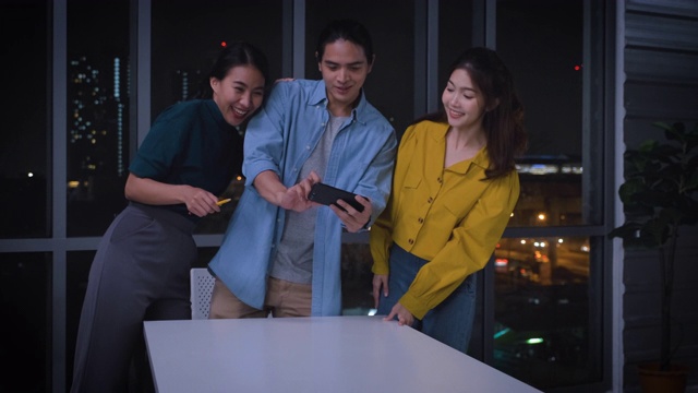 亚洲用户体验开发人员和ui设计师在城市灯光下的现代办公室里研究增强现实(ar)手机应用原型设计。创意数字发展机构视频素材