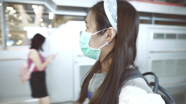 亚洲妇女戴着面具在机场候机楼行走的场景视频素材