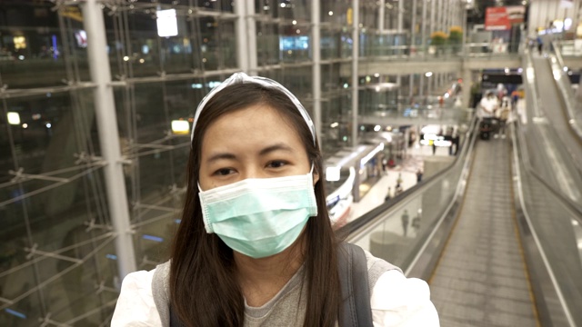 一名亚洲女子戴着面具站在机场的自动扶梯扶手上视频素材