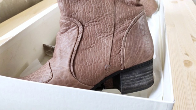棕色的女靴躺在白色的盒子里。从盒子里拿出带后跟的皮鞋，小尘埃飞扬视频素材