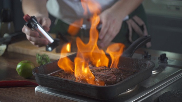 厨师在烤盘上制作火焰风格的牛排。油和酒精用明火燃烧。在烹饪食物。营养在美食厨房。做顿饭。准备吃的食物。美味的菜。视频素材