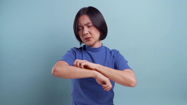 亚洲妇女抓她的皮肤站在孤立的蓝色背景。4 k的视频视频下载
