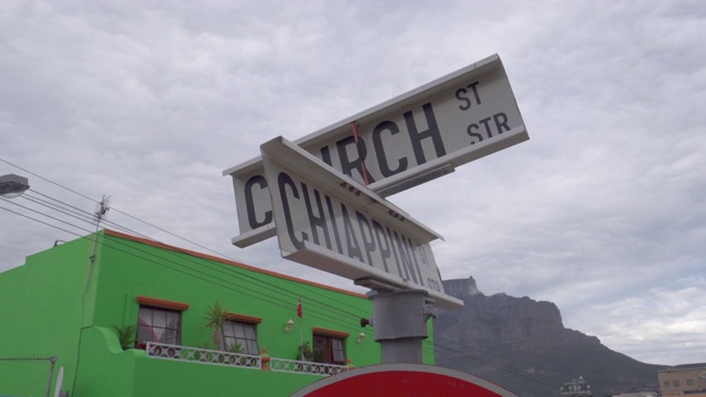 在一个阴天，一个缓慢的特写镜头拍摄了博卡普的一个弯曲的街道标志，背景是一座绿色建筑——南非开普敦视频下载
