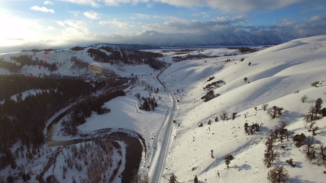 鸟瞰河中积雪覆盖的道路和常青树，风景的白色山脉对天空日落-杰克逊，怀俄明州视频购买