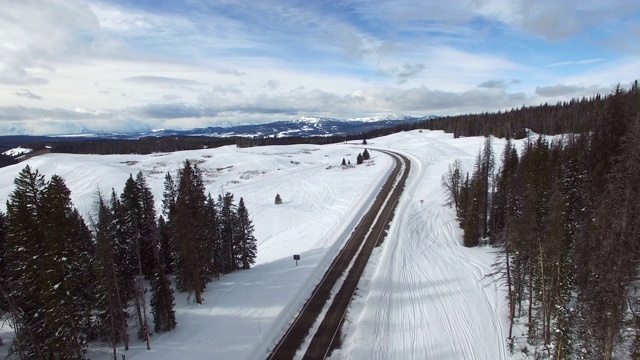 空旷的公路鸟瞰图在常青树在雪，无人机下降的道路对天空在冬天-杰克逊，怀俄明州视频素材