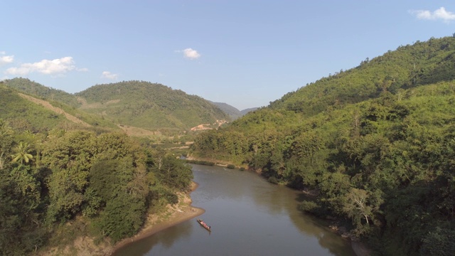 空中拍摄的船在河中树木对天空，无人机从绿色的山向后飞行在阳光明媚的一天-湄公河，老挝视频素材