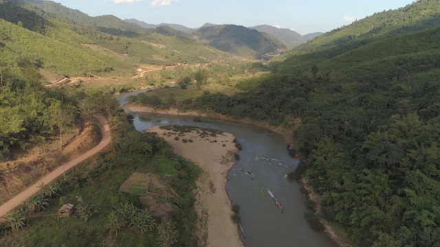 航拍的河流上的船在森林中附近的道路在山谷，无人机从树木和山脉向后飞行的天空-湄公河，老挝视频素材