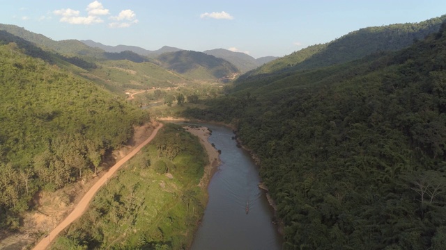 航拍河上的船在绿树中靠近道路，无人机从森林和山脉向后飞行的天空-湄公河，老挝视频素材