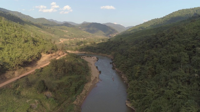 航拍的河流上的船在树林中附近的道路在山谷，无人机飞向后从森林和山脉的天空-湄公河，老挝视频素材