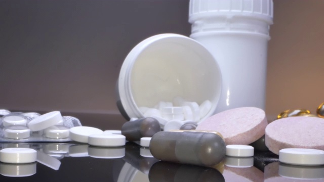 治疗理念，包装和罐子里的药物和药片散落在黑色的桌子上视频下载