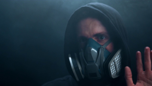 在黑暗的背景上，一个戴面具的人在他周围的烟雾中跳舞。视频下载