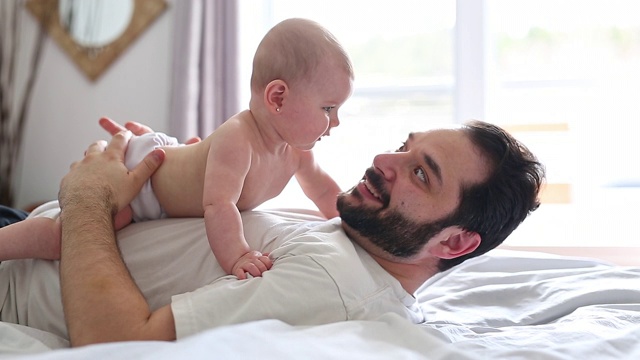 年轻快乐的父亲和婴儿在床上玩视频素材