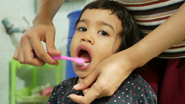 亚洲母亲在浴室里给她的学龄前可爱的小女孩刷牙视频素材