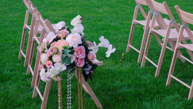 在刮风的日子里，绿色草地上放着花束和白色的木制空椅子。婚礼装饰。视频素材