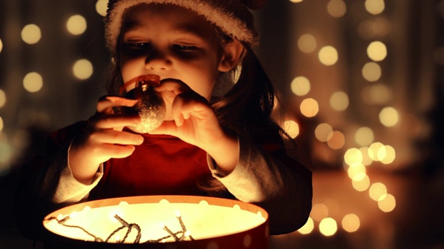 小女孩从一个发光的礼品盒里拿出一个圣诞装饰品视频素材