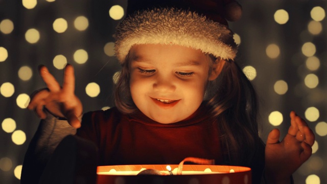 快乐的小女孩正在玩她在一个发光的礼品盒里找到的圣诞装饰品视频素材