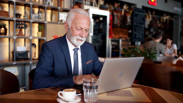 现代高级商人在咖啡店用笔记本电脑做一个工作项目视频素材