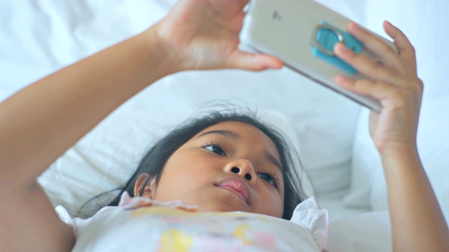 快乐的小女孩在卧室用手机。视频素材