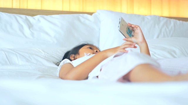 快乐的小女孩在卧室用手机。视频素材