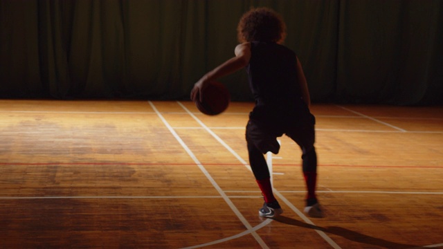 年轻卷曲的职业篮球运动员在打拼球时把球投进篮里，夜深人静，训练运球视频下载