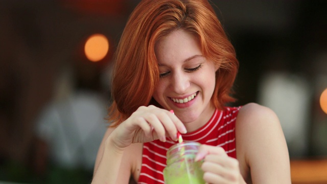 漂亮女孩喝绿色果汁。红头发的年轻女子拿着排毒饮料微笑和大笑视频素材