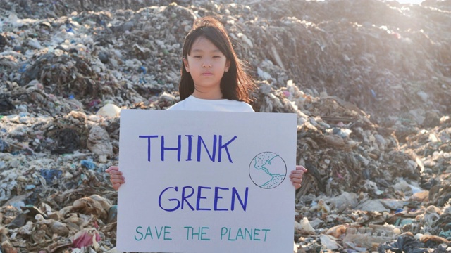 描绘一个年轻的亚洲小女孩站在一个巨大的垃圾堆上，从亚洲的垃圾填埋场拿着为环保运动积极分子争取自然的海报。志愿服务，慈善，清洁，人，儿童，生态概念，儿童关于可持续发展。视频素材