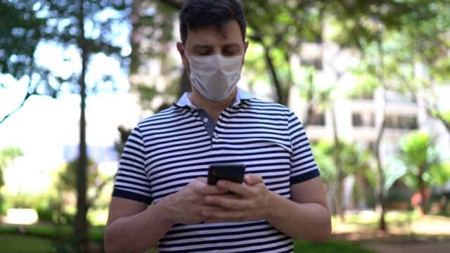 一名男子在公园里用手机行走，还戴着口罩视频下载